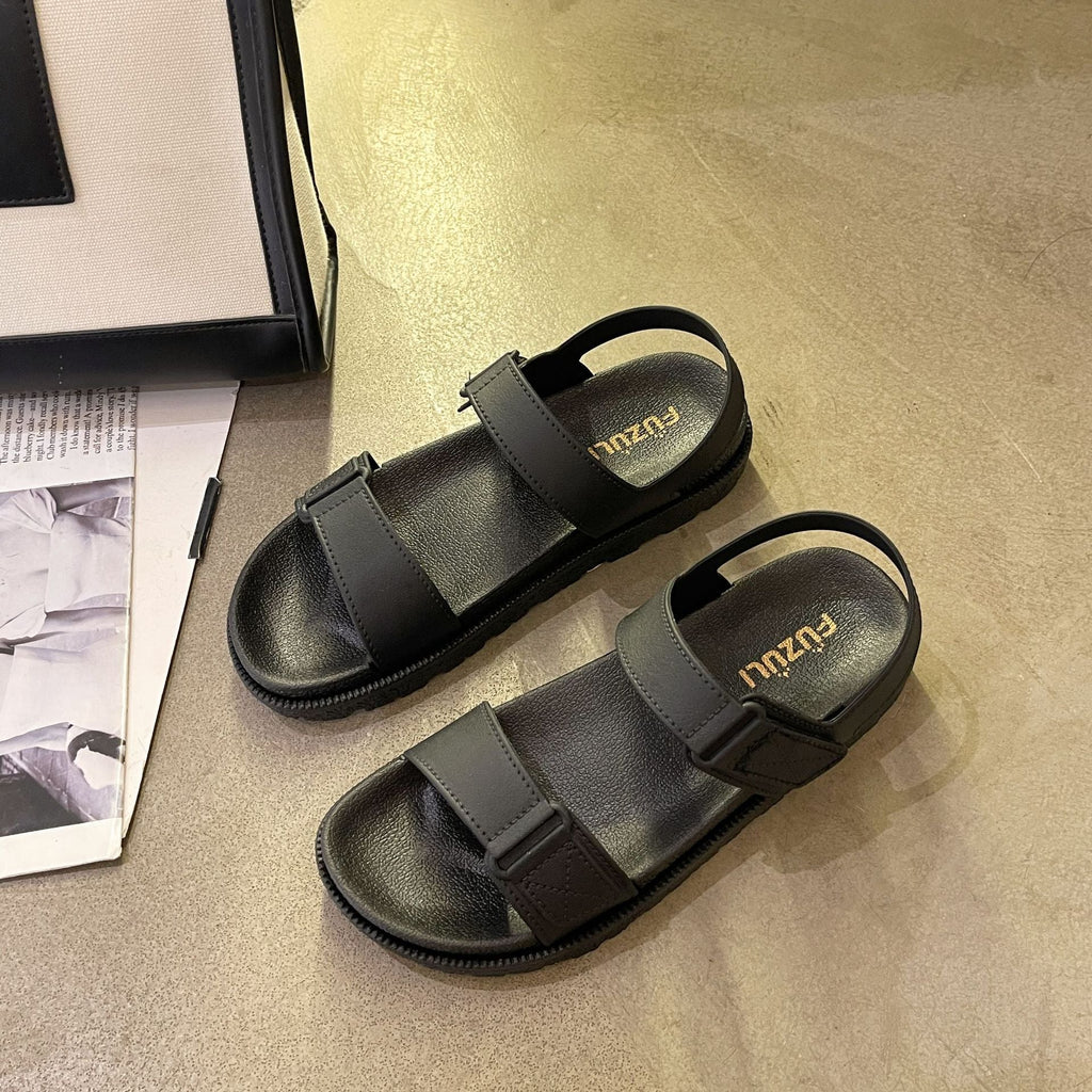Sorte flade sandaler med tyk sål og velcroremme set fra siden på gulv — Venzelo