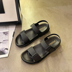 Sorte flade sandaler med tyk sål og velcroremme set fra siden på gulv — Venzelo