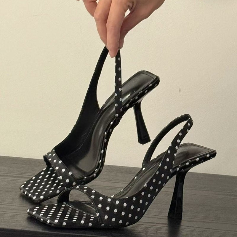 Sort prikket slingback sandal med hvide prikker og firkantet tå holdt op — Venzelo