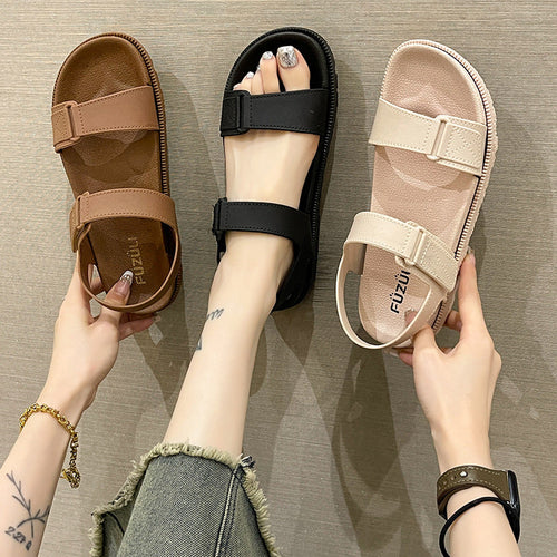 Sort, cognac og beige flade sandaler med velcrolukning holdt frem mod grå baggrund — Venzelo