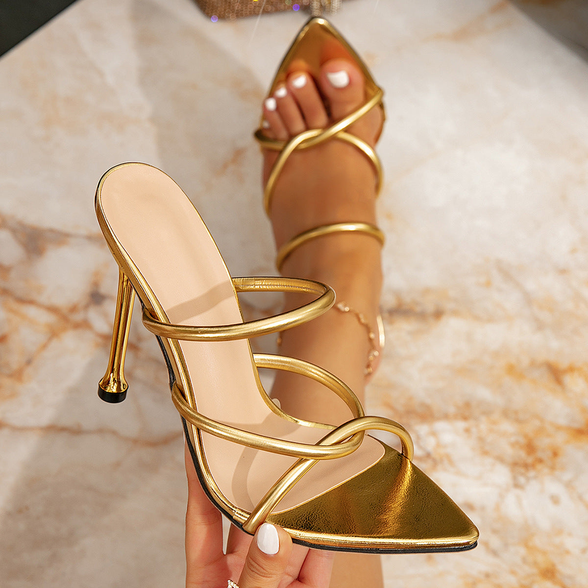 Guld stiletsandal med krydsende rørremme og spids tå holdt i hånden — Venzelo