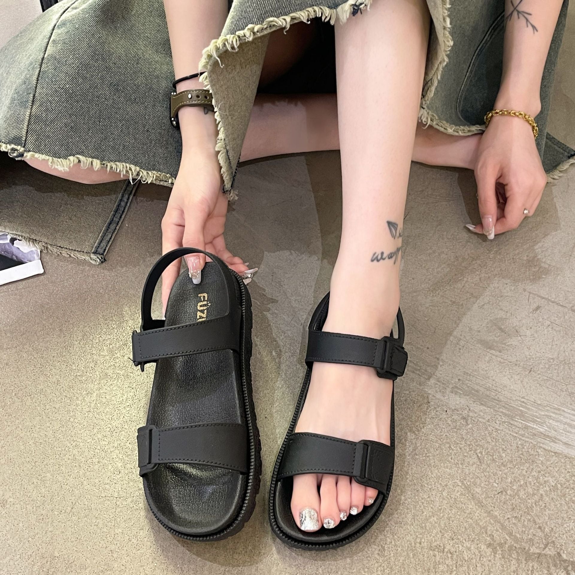 Sort sandal holdt i hånden ved siden af fod iført sort sandal med tyk sål — Venzelo